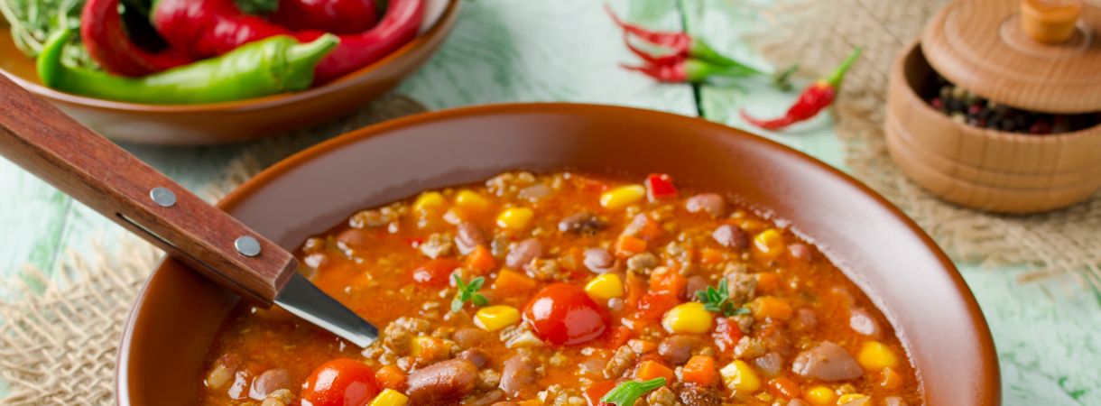 Bowl of chilli with a spoon in it, little chilis on the side on the table.