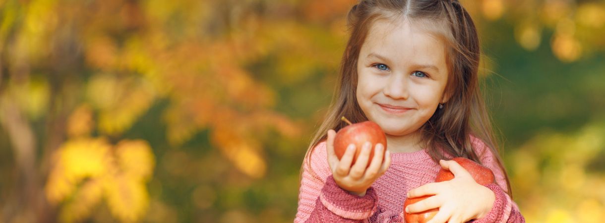 Girl holding three apples with fall foliage in the background